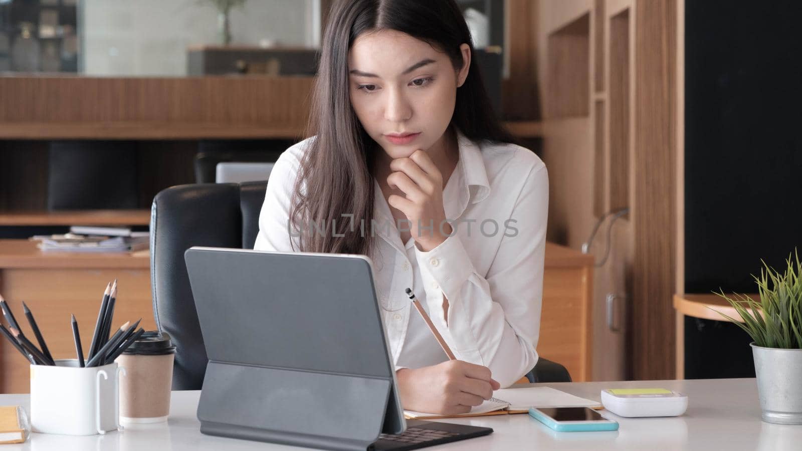 Photo of cheerful joyful asian woman writing down notes holding tablet for data analysis 
