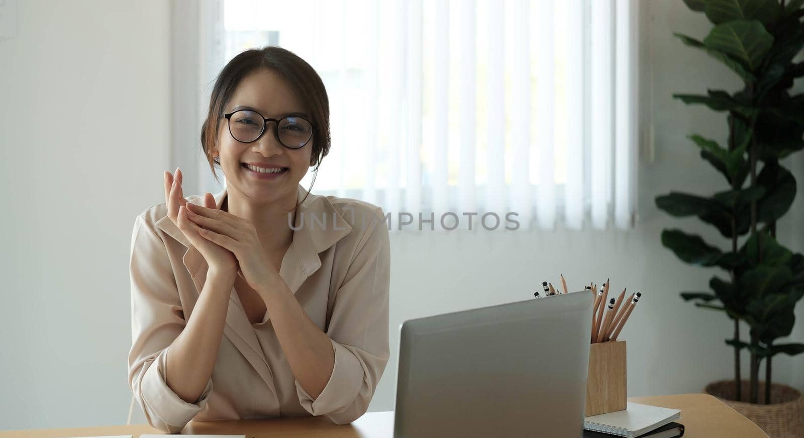 Portrait of smiling businesswoman sitting at desk in the office working on laptop by wichayada