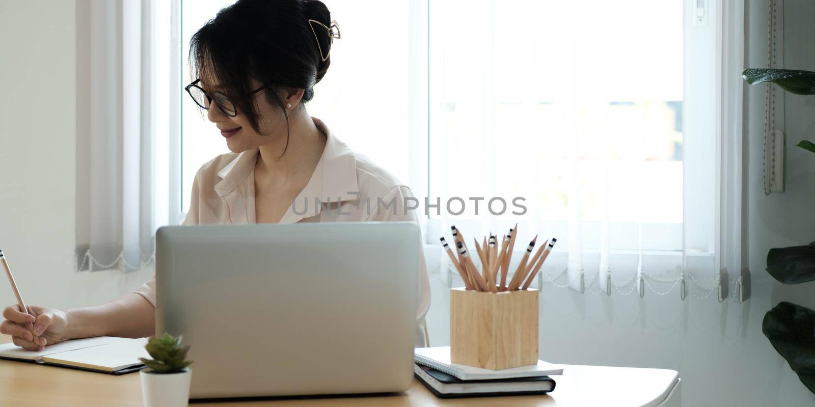 Woman make notes sit at work desk while study online watching webinar podcast on laptop listening learning education course conference, elearning concept by wichayada