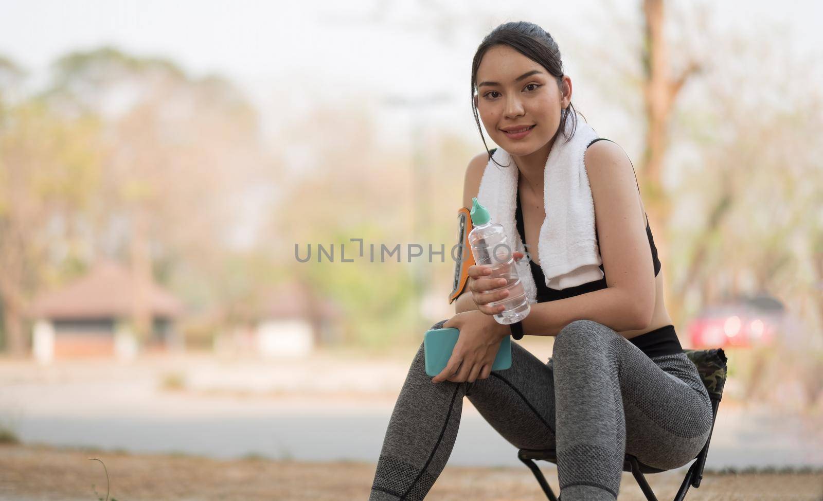 Young athletic woman holding water from a bottle after running in the park.