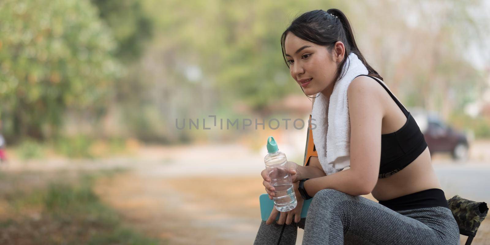 Young athletic woman holding water from a bottle after running in the park by nateemee