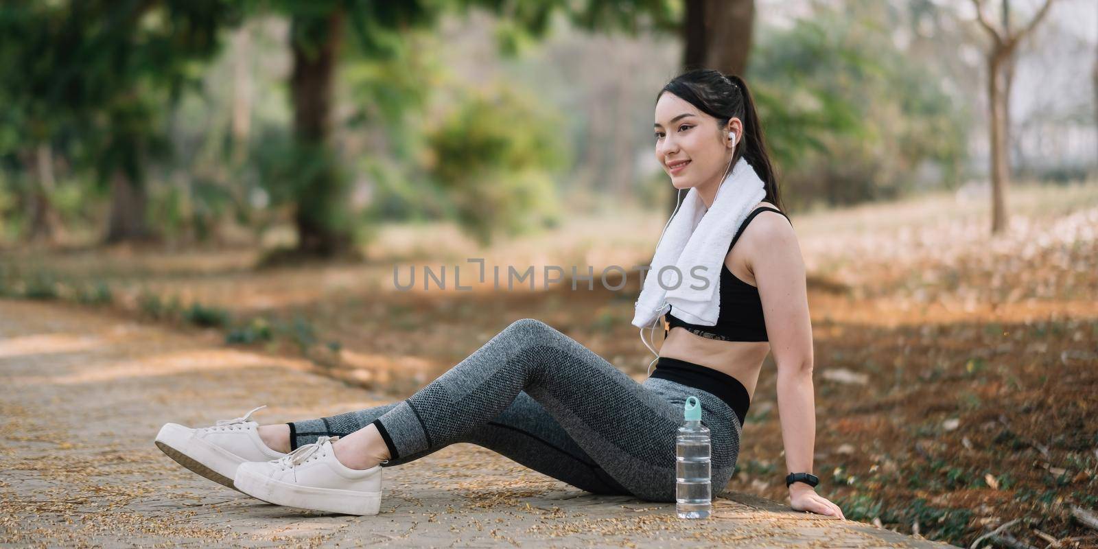 Athletic asian woman resting after a hard training in the mountains at sunset. Sport tight clothes.