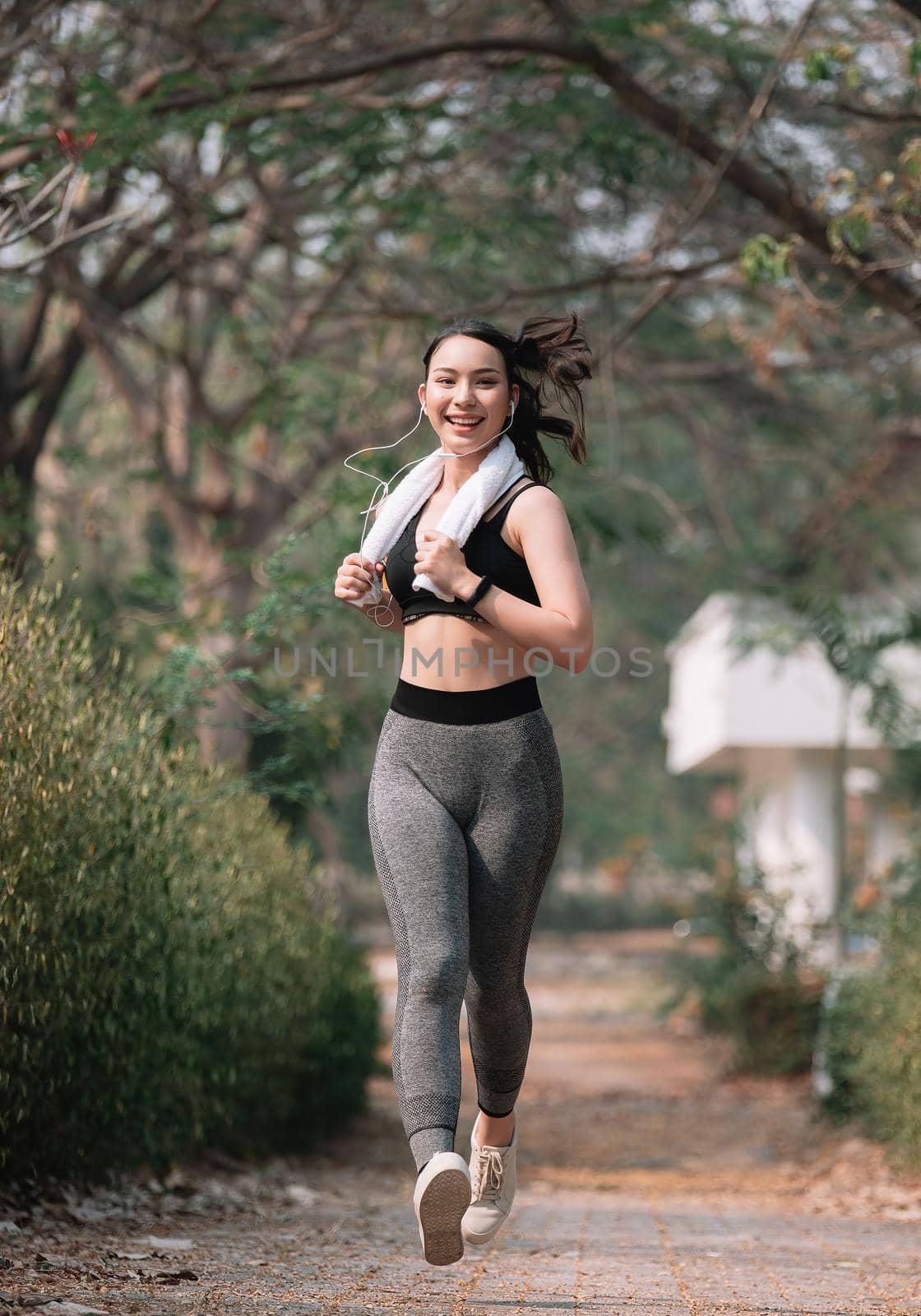 Sporty asian young woman running on park road in beautiful nature.