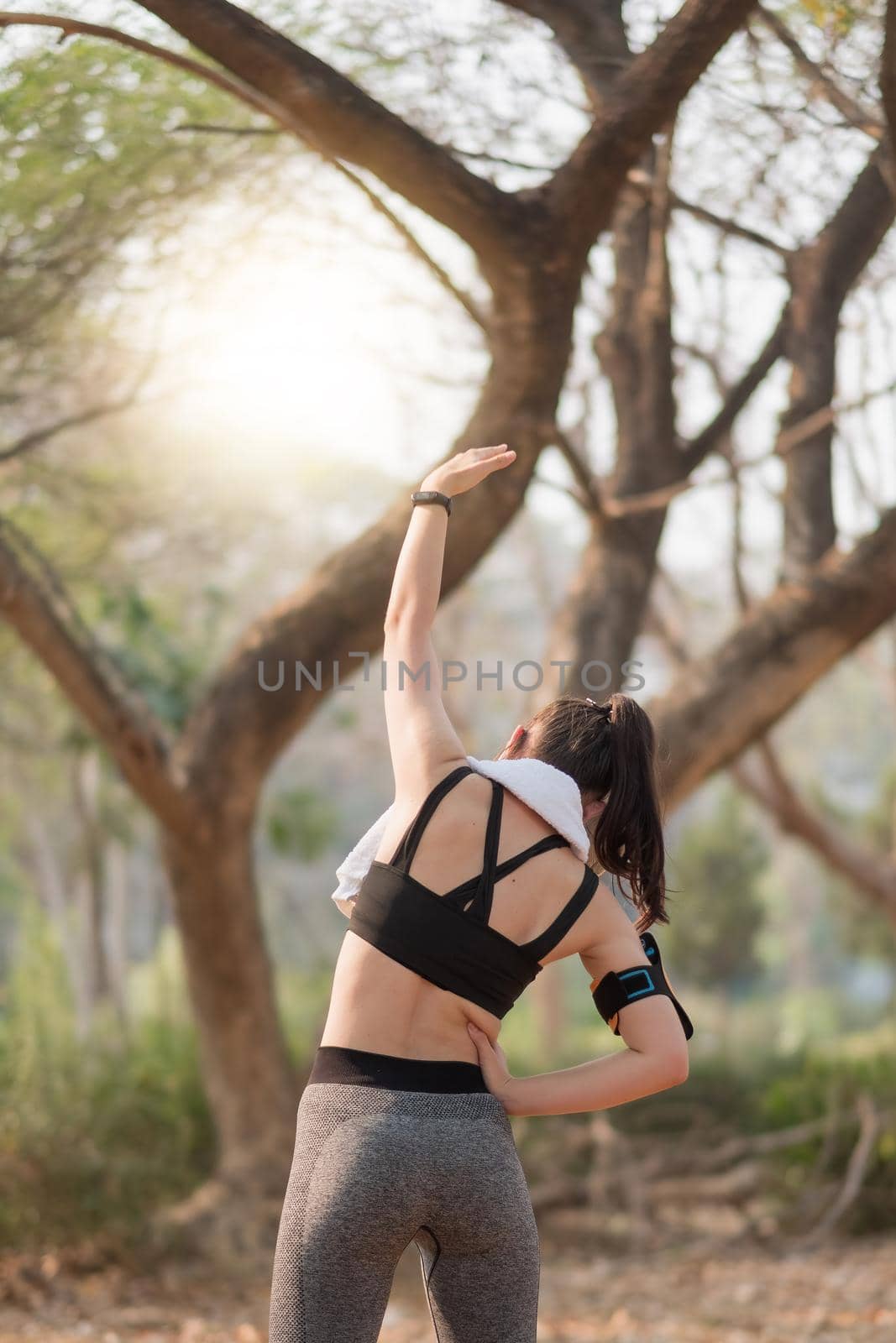 Athletic woman warming up before a workout standing facing the early morning rising sun at park.