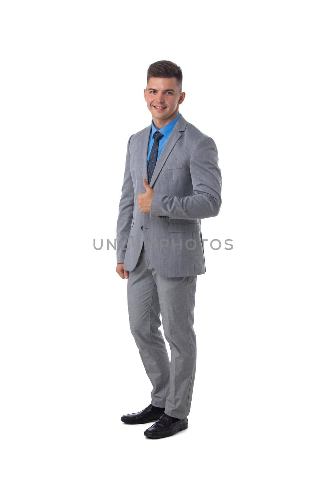 Full length portrait of a young business man in gray suit holding thumbs up isolated on white background