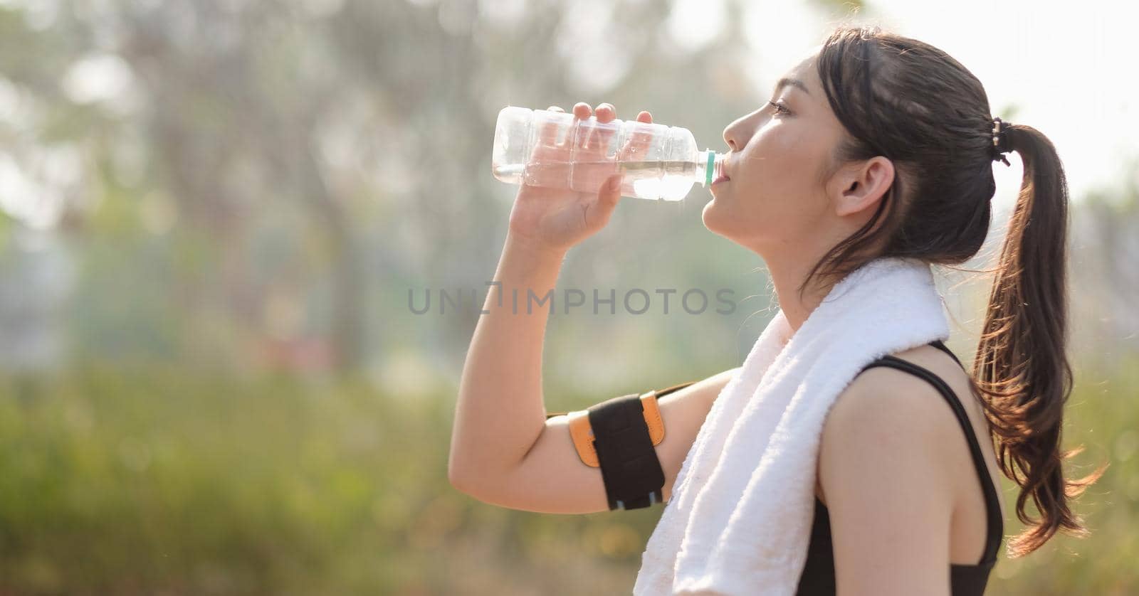 Beautiful fitness athlete woman drinking water after work out exercising on sunrise morning summer in park.