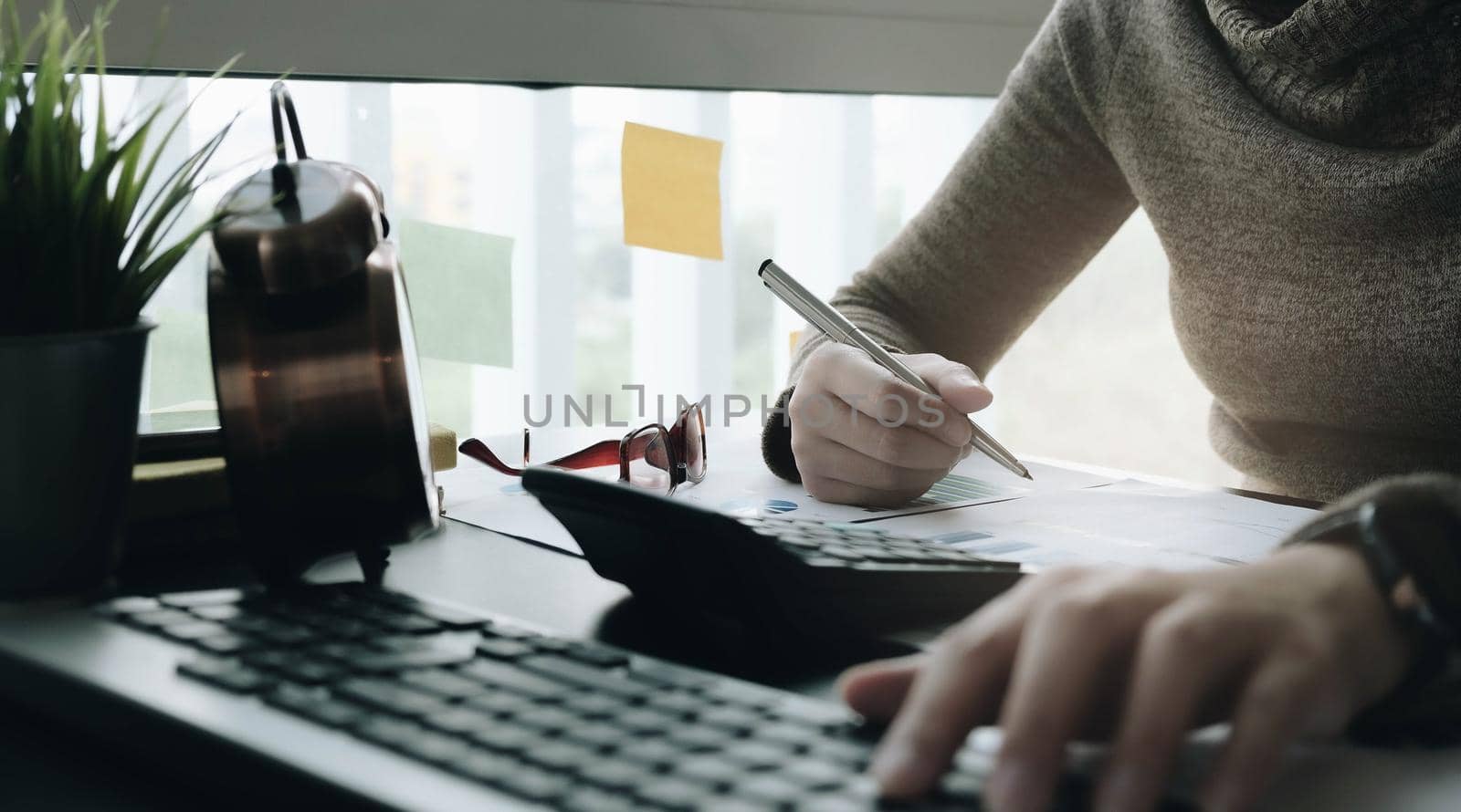 Close up of businessman or accountant hand holding pencil working on calculator to calculate financial data report, accountancy document and laptop computer at office, business concept
