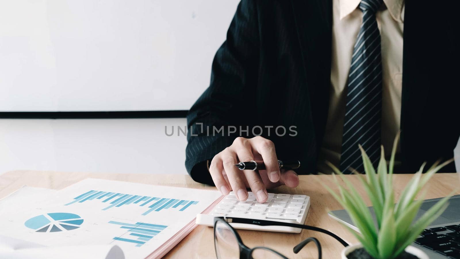 Close up of businessman or accountant hand holding pen working on calculator to calculate business data, accountancy document and laptop computer at office, business concept
