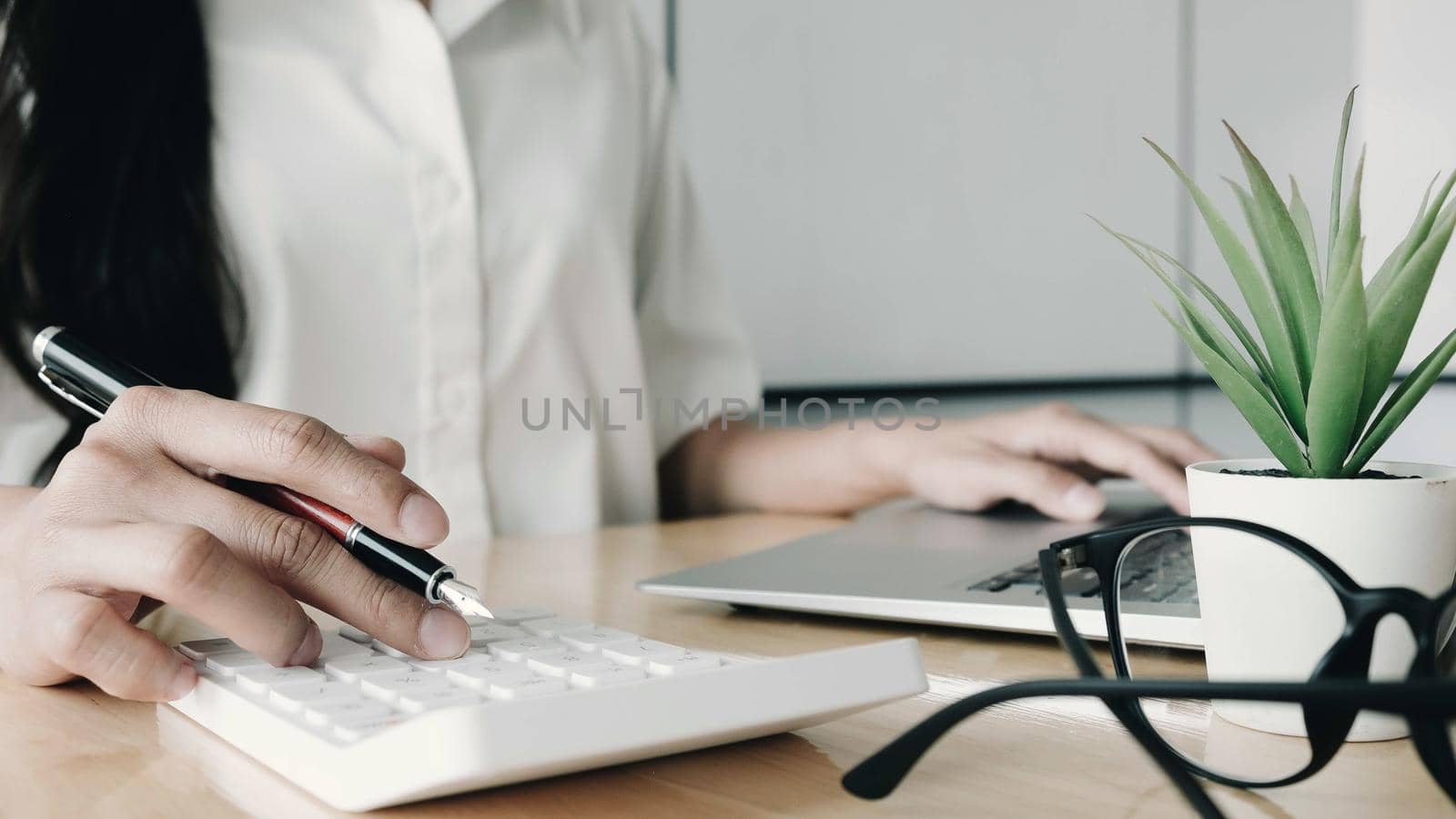 Close up Business woman using calculator and laptop for do math finance on wooden desk in office and business working background, tax, accounting, statistics and analytic research concept

