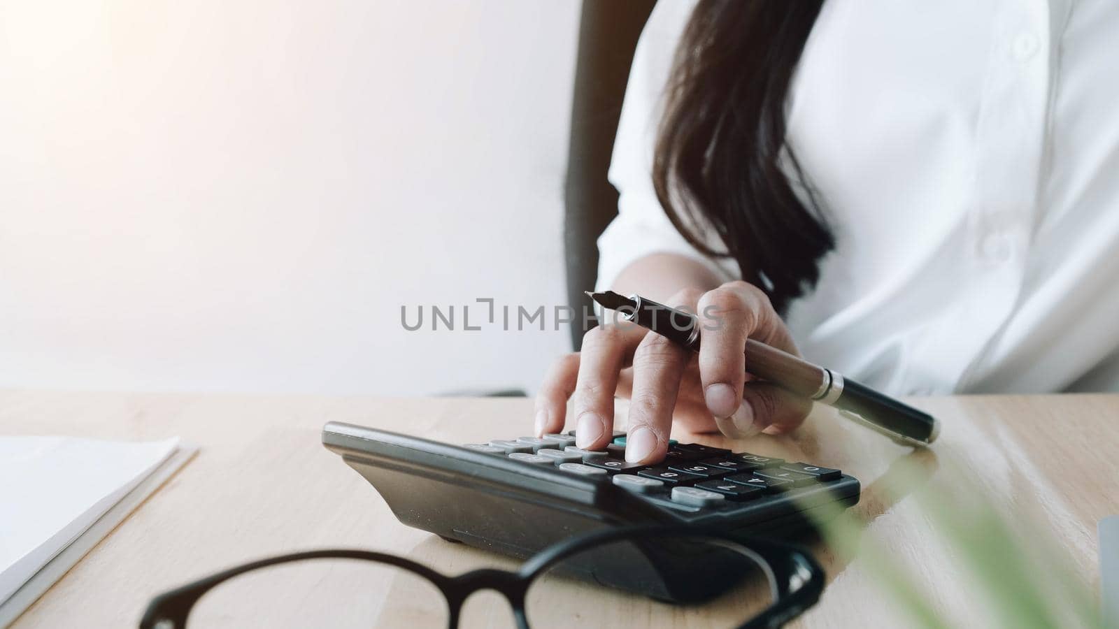 Close up of businesswoman or accountant hand holding pen working on calculator to calculate business data, accountancy document and laptop computer at office, business concept
