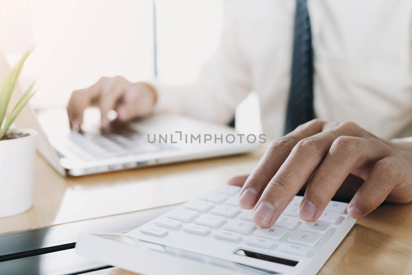 Close up Businessman using calculator and laptop for do math finance on wooden desk in office and business working background, tax, accounting, statistics and analytic research concept
