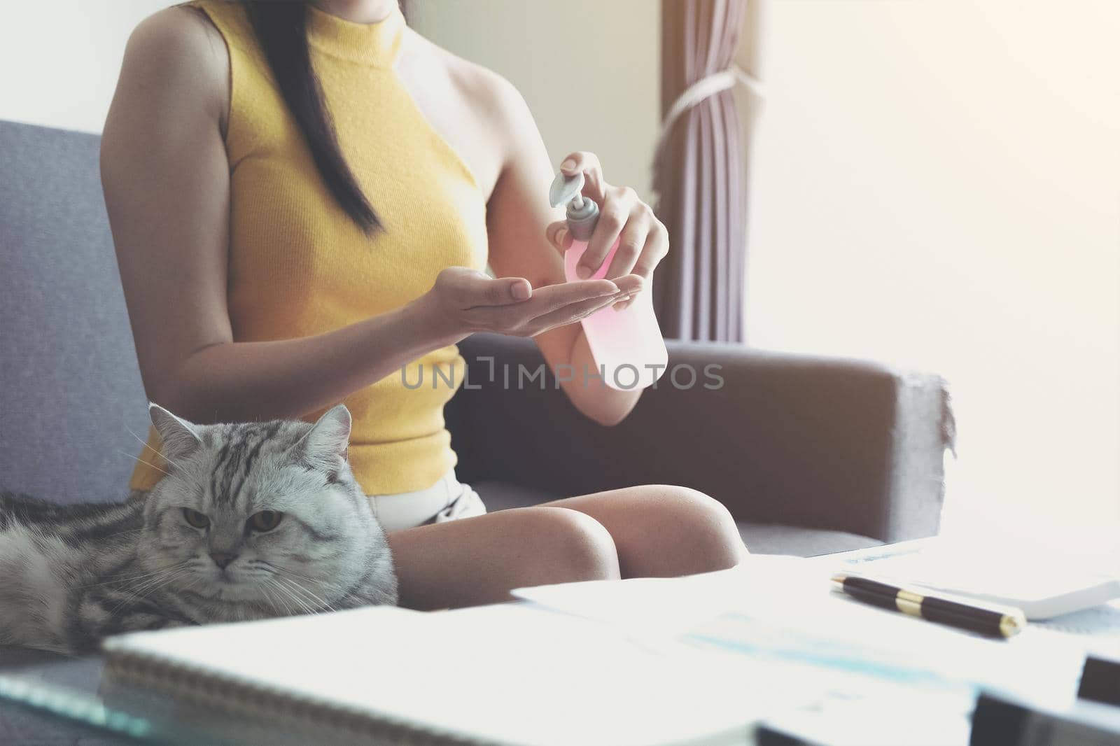 Young woman sit at sofa and using algohol gel or hand sanitizer for wash her hand. Concept work from home and social distancing from covid-19 by wichayada
