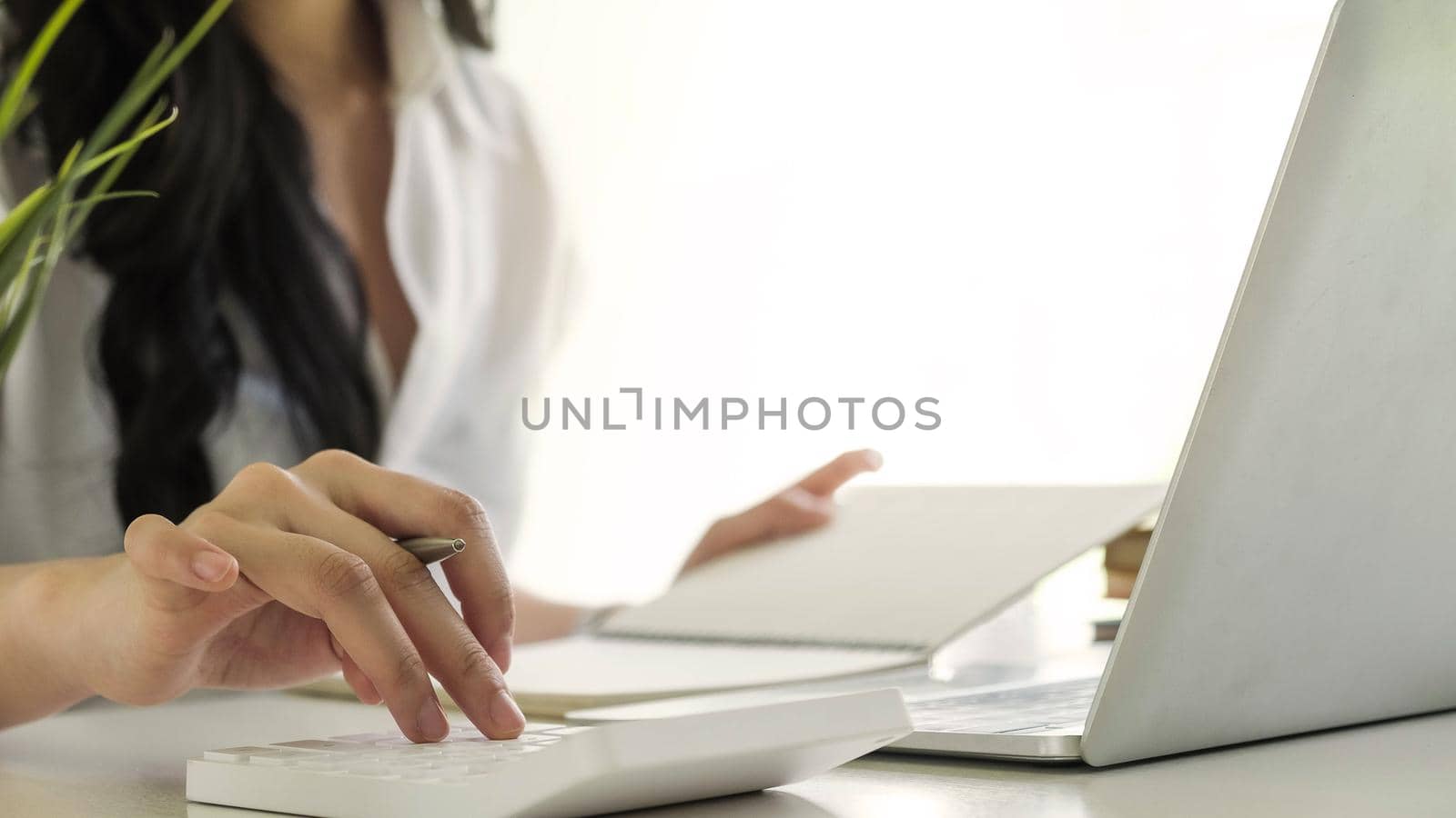 Close up of busineswosman or accountant hand holding pen working on calculator to calculate business data, accountancy document and laptop computer at office, business concept	