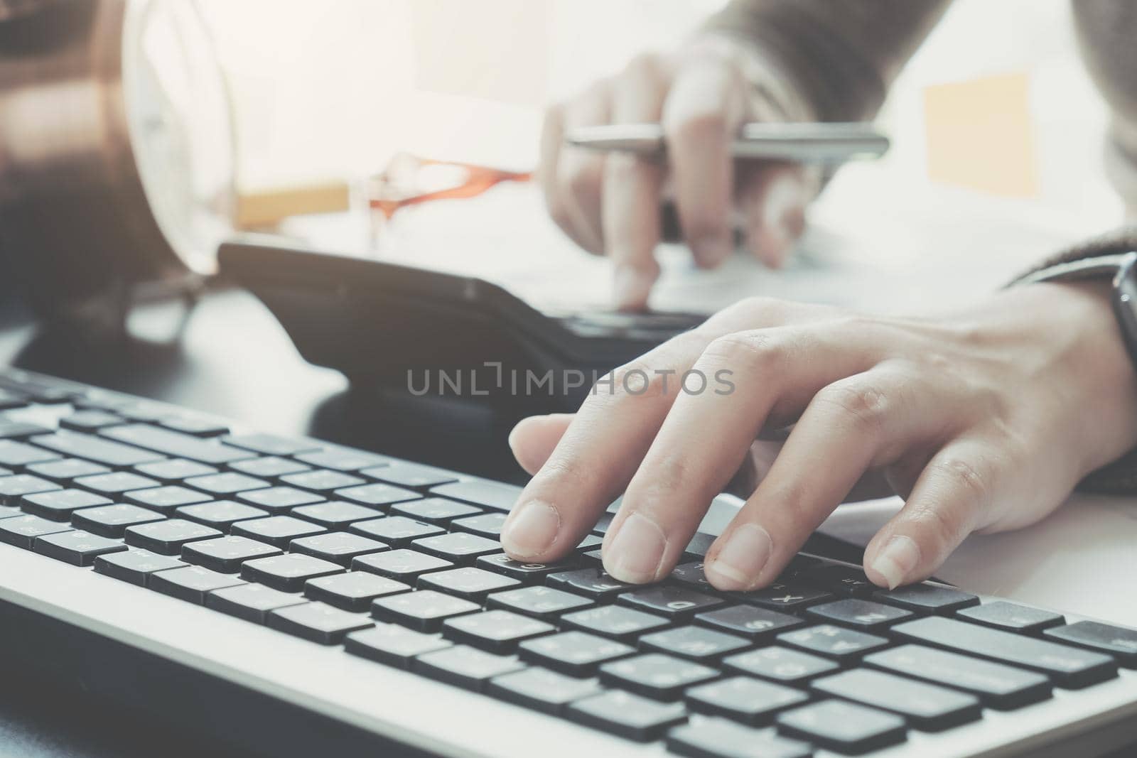 Close up of businessman or accountant hand holding pen working on calculator to calculate business data, accountancy document and laptop computer at office, business concept by wichayada