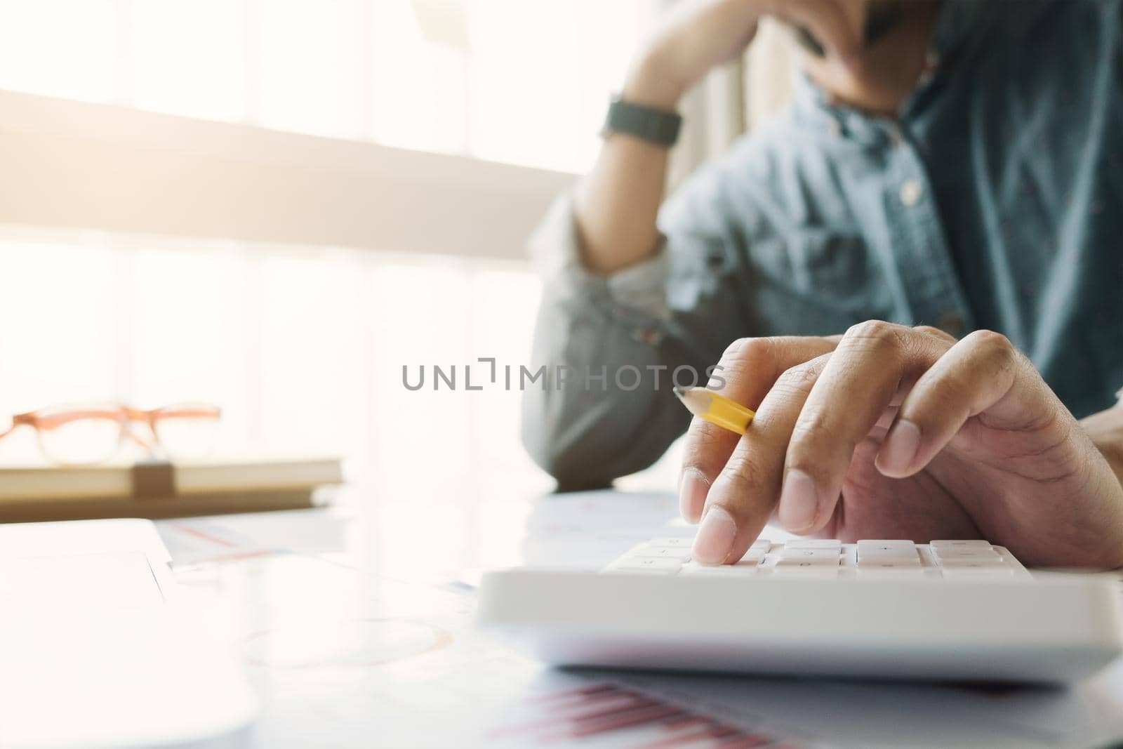 Close up of businessman or accountant hand holding pen working on calculator to calculate business data, accountancy document and laptop computer at office, business concept by wichayada