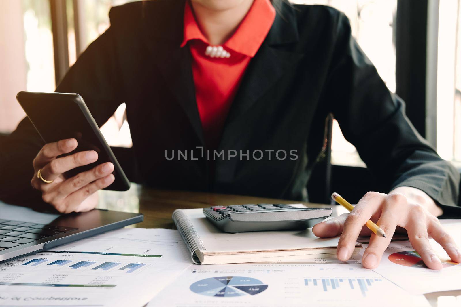 Woman write on notebook and holding mobile phone with laptop. by wichayada