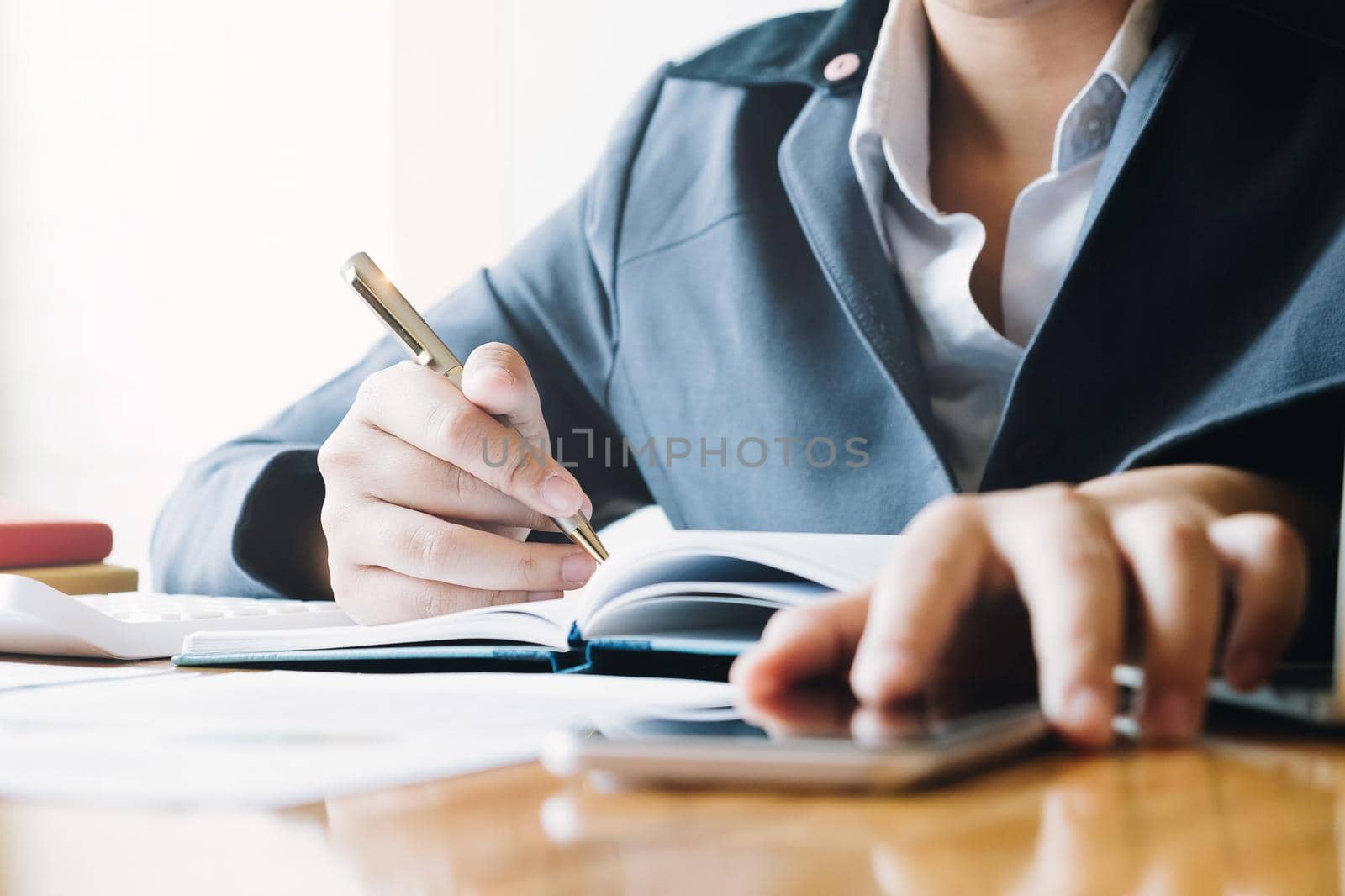 Businesswoman working on smartphone and writing down notes on notebook. Business planning and organization, paperwork concept by wichayada