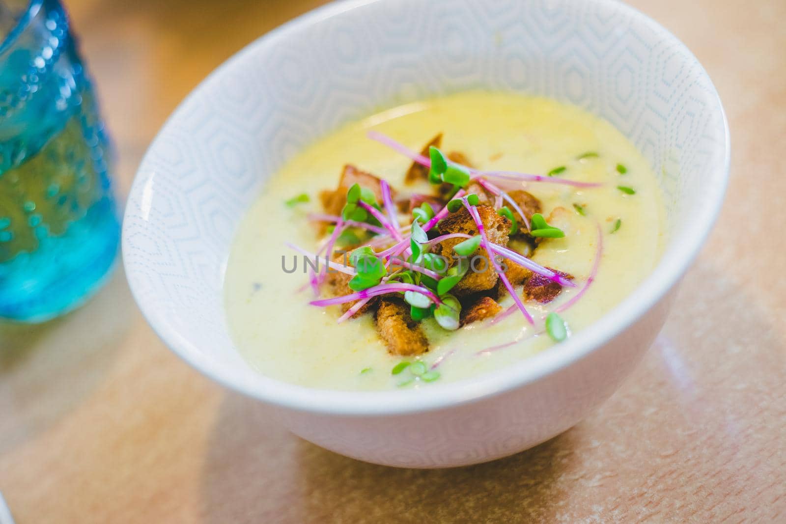 Close up of fresh broccoli soup with crunchy croutons and radish sprouts in white ceramic bowl