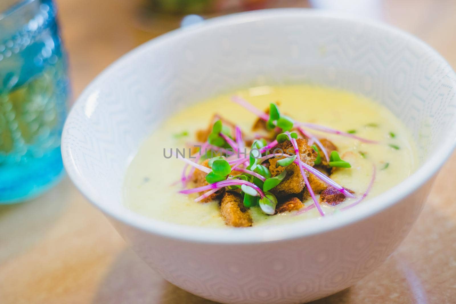 Close up of fresh broccoli soup with crunchy croutons and radish sprouts in white ceramic bowl