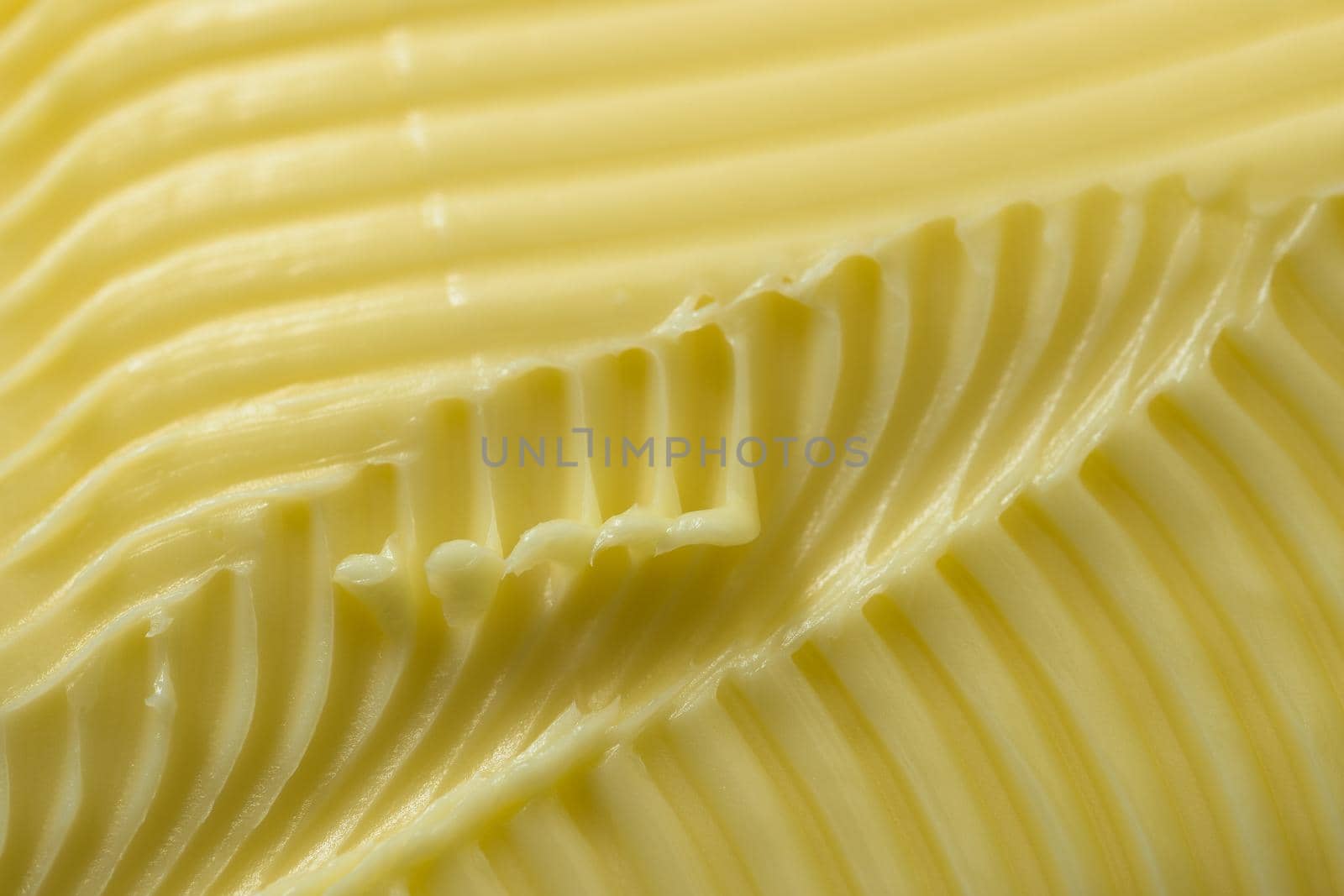 Close up of yellow butter. Full frame textured background, with a super macro perspective. Serrated butter knife used to create the abstract patterns
