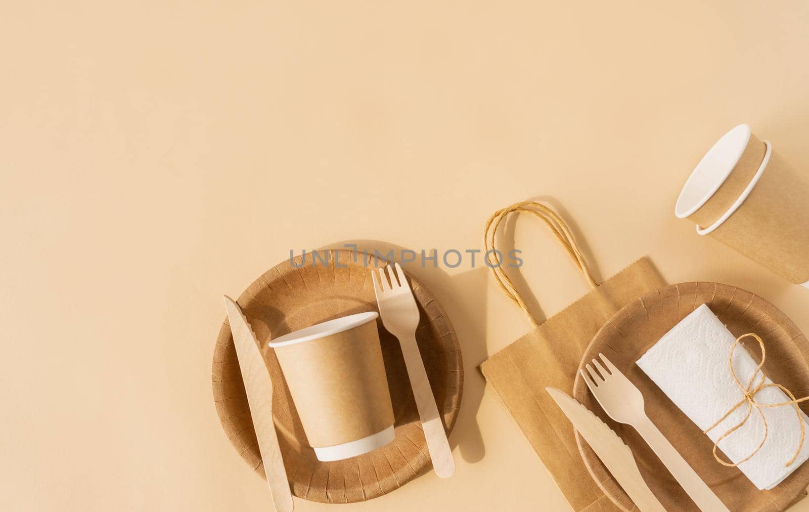 Reusable, disposable and recycling concept. Brown craft disposable bag and tableware cup, plate, and wooden fork, knife on brown background flat lay top view