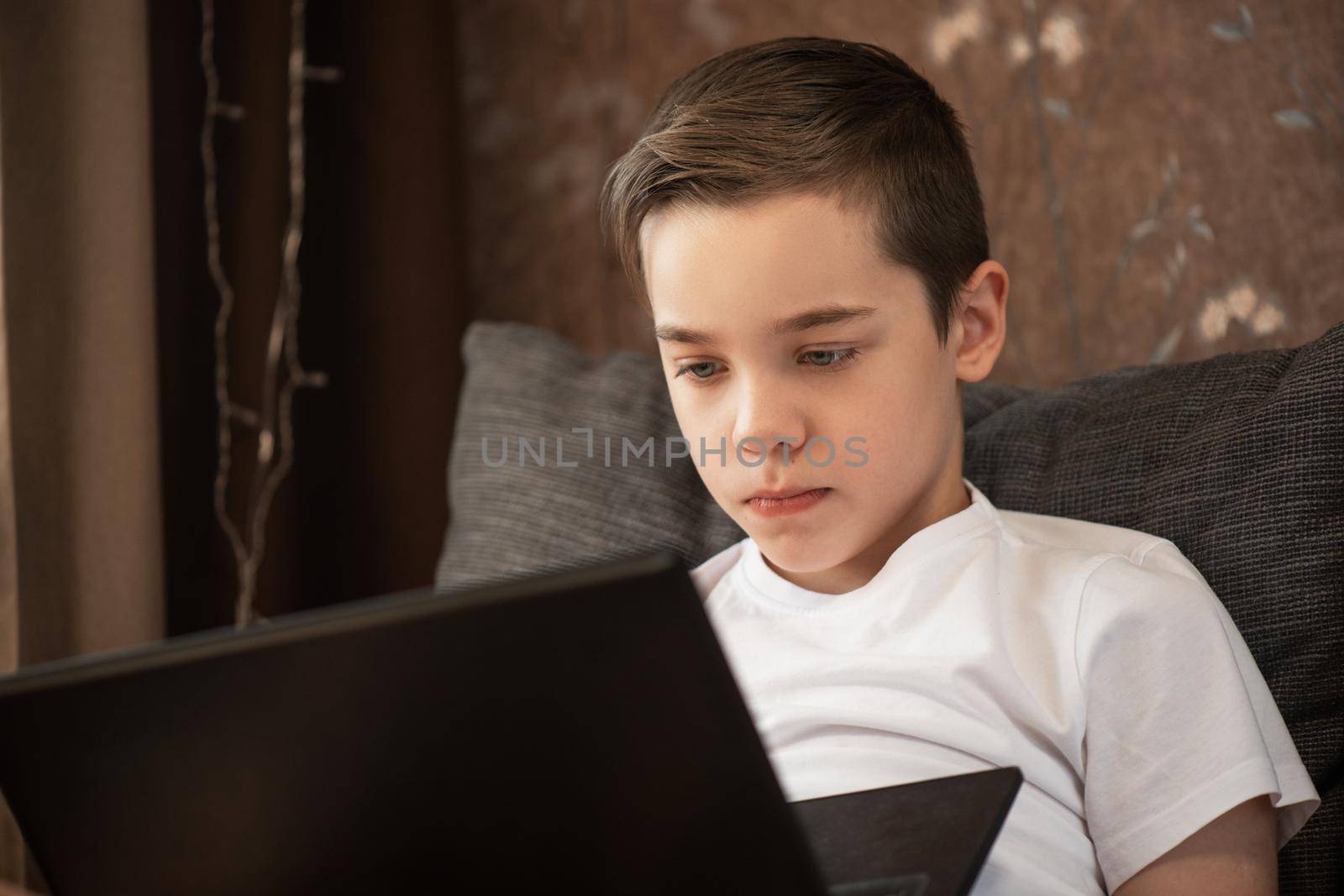Kid boy or teen learning at home on laptop for school. Adorable child making homework and using notebook. Home schooling concept.