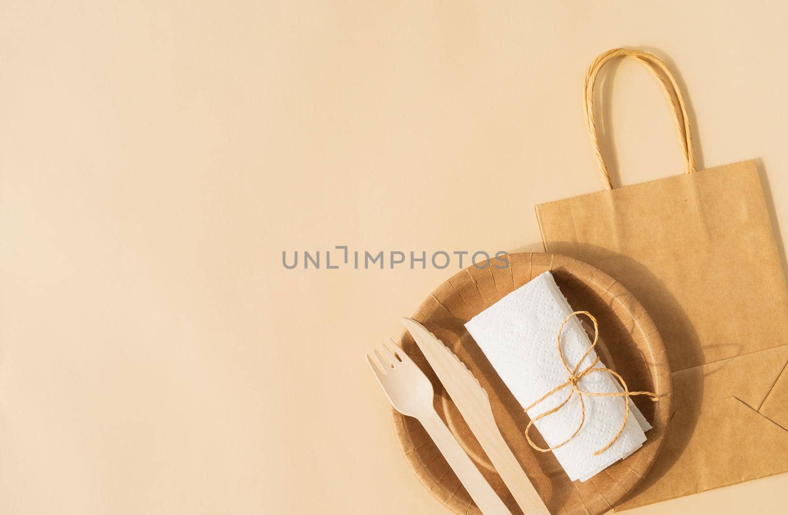 Reusable, disposable and recycling concept. Brown craft disposable bag and tableware cup, plate, and wooden fork, knife on brown background flat lay top view