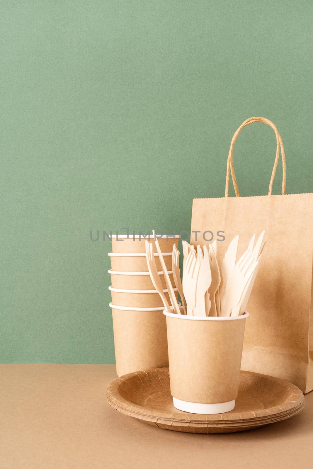 Reusable, disposable and recycling concept. Disposable eco friendly tableware on green background: paper bag, cups, forks and knives