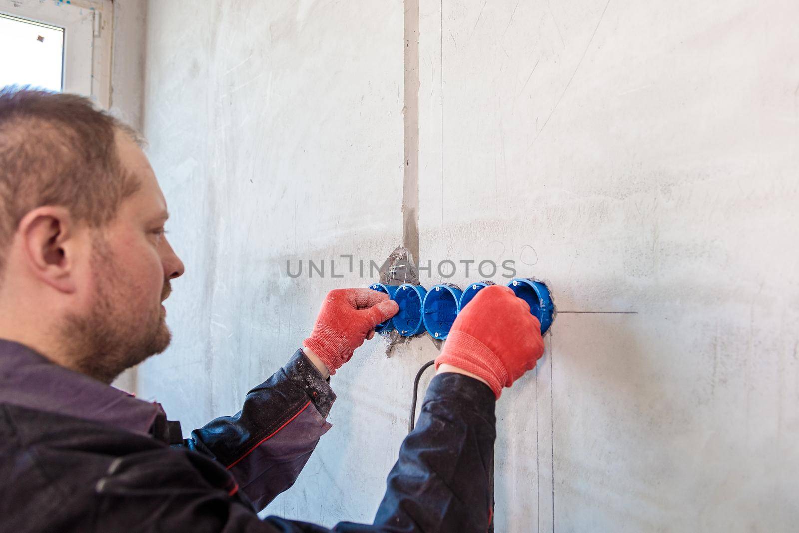 The electrician inserts the plastic box directly into the outlet holes. Close-up