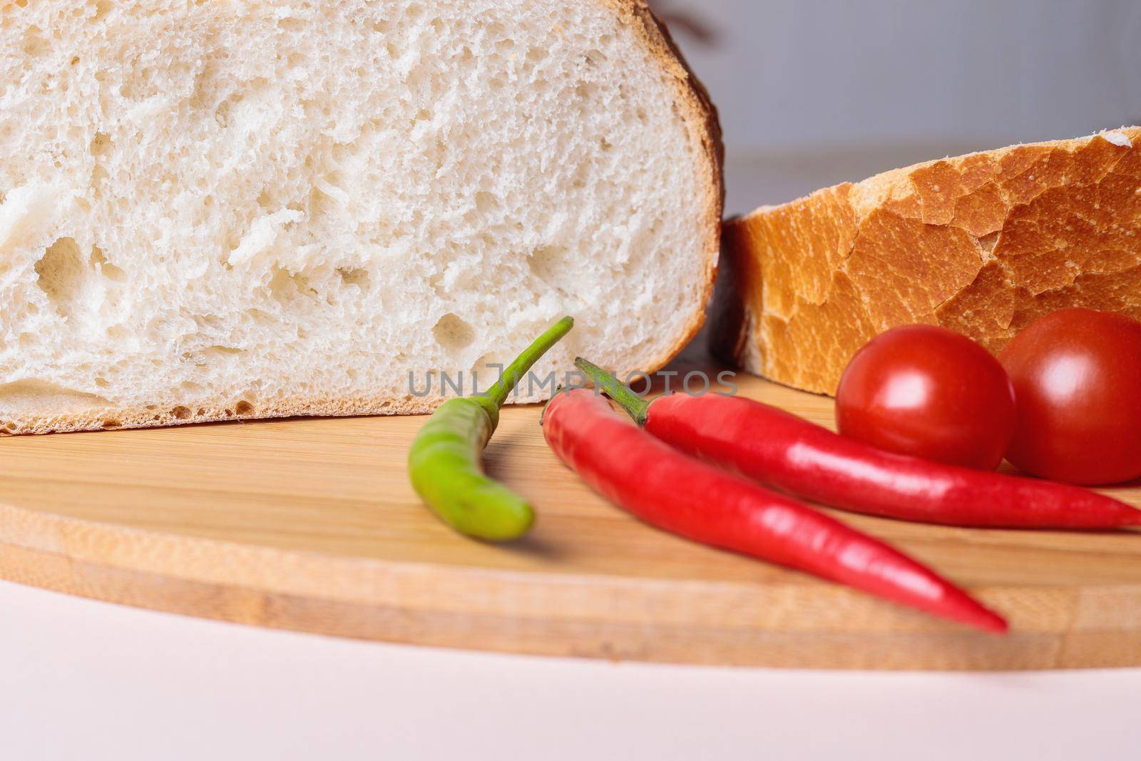Sliced pieces of white bread with red peppers and tomatoes on a cutting board. Light background