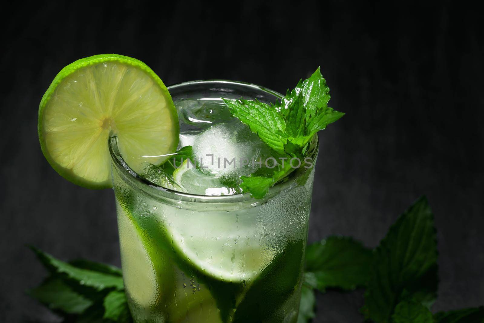 Fresh homemade mojito cocktail with lime, mint and ice on a black background, close-up, copy space.