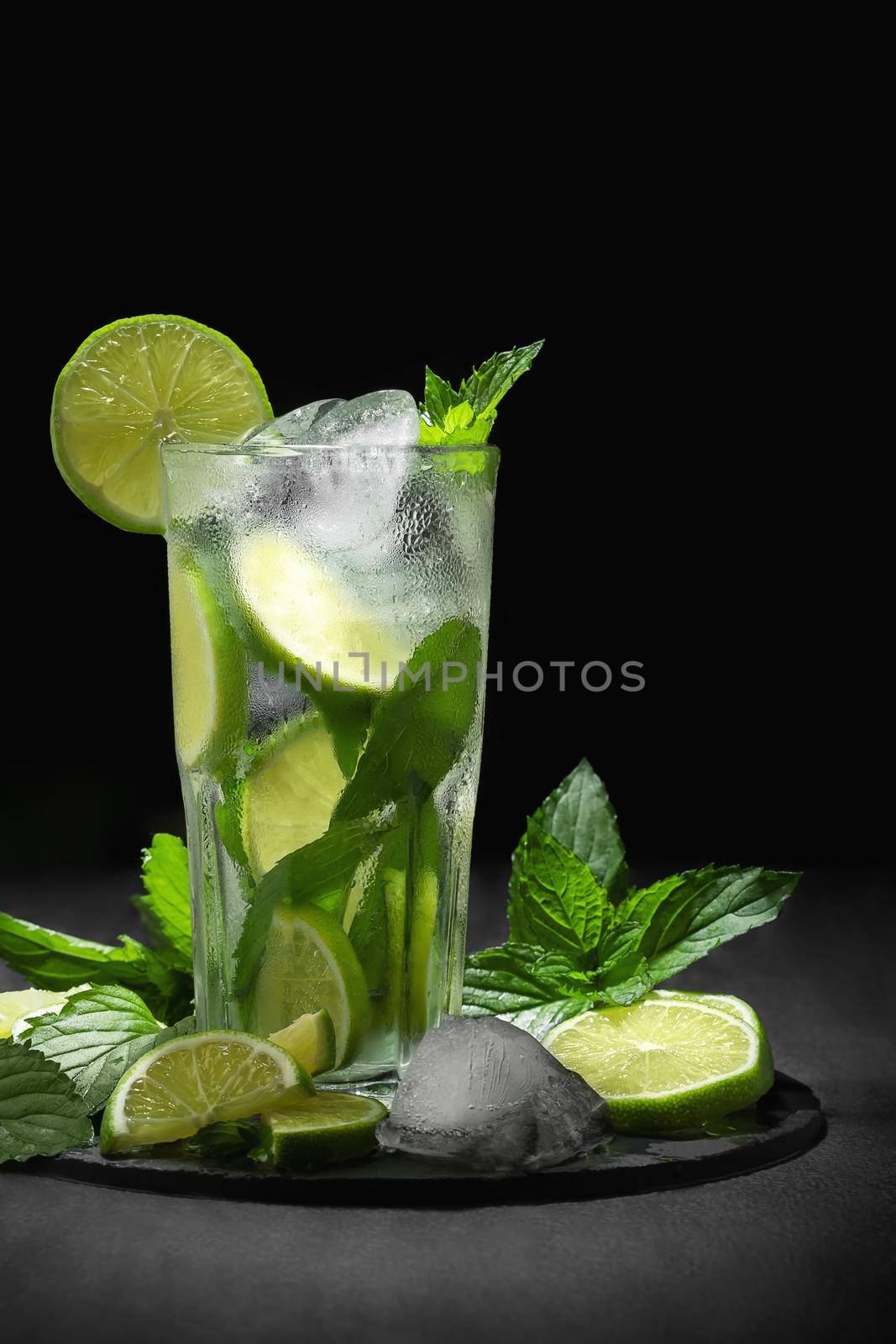 Fresh homemade mojito cocktail in a tall glass with lime, mint and ice on a black background, copy space, vertical image by galsand