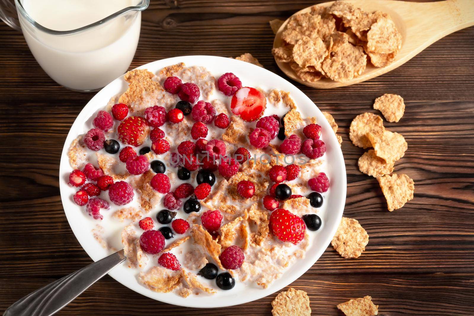 A bowl of cereal and berries with milk on a wooden table. Healthy summer breakfast by galsand