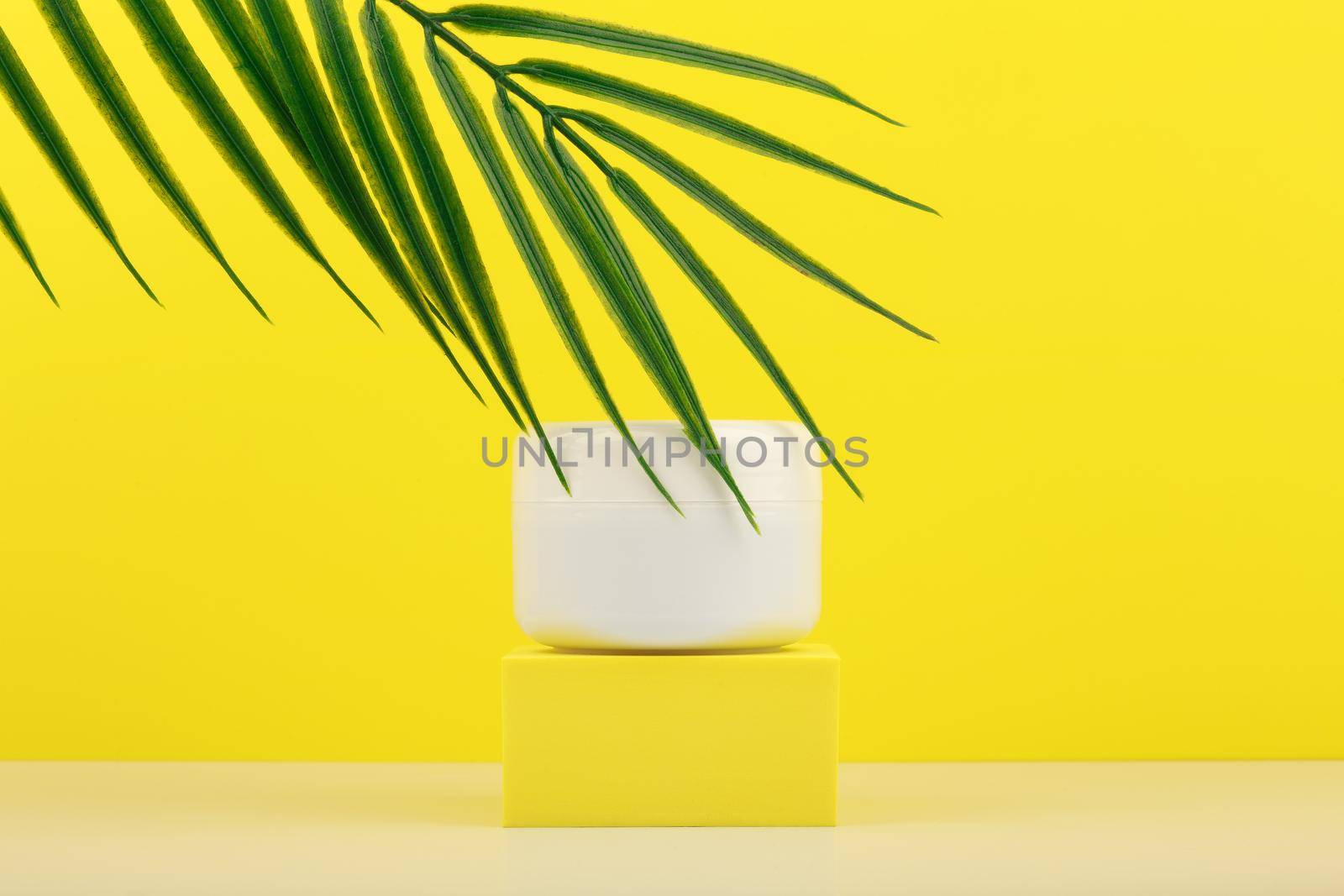 White cosmetic jar on yellow podium against yellow background with palm leaf and space for text by Senorina_Irina