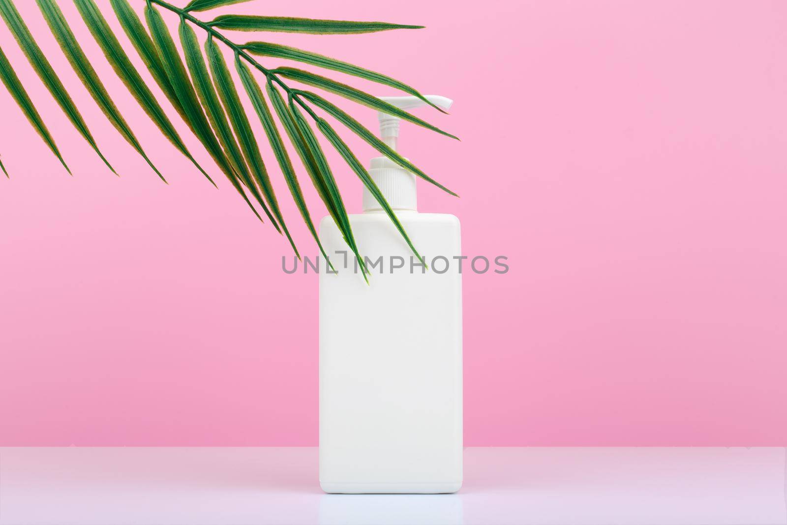 Body cream in tall white tube with dispenser against pink background with palm leaf and copy space.Concept of body care and beauty products for moisturizing, hydration and exfoliation 