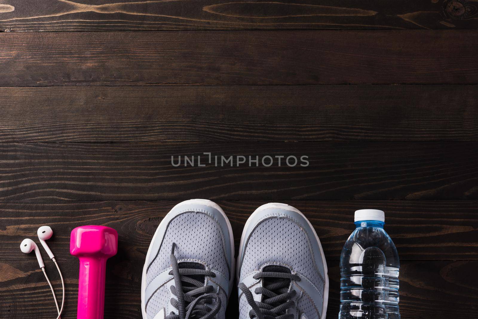 Pair sports shoes, headphones, dumbbell and water bottle on black wood by Sorapop