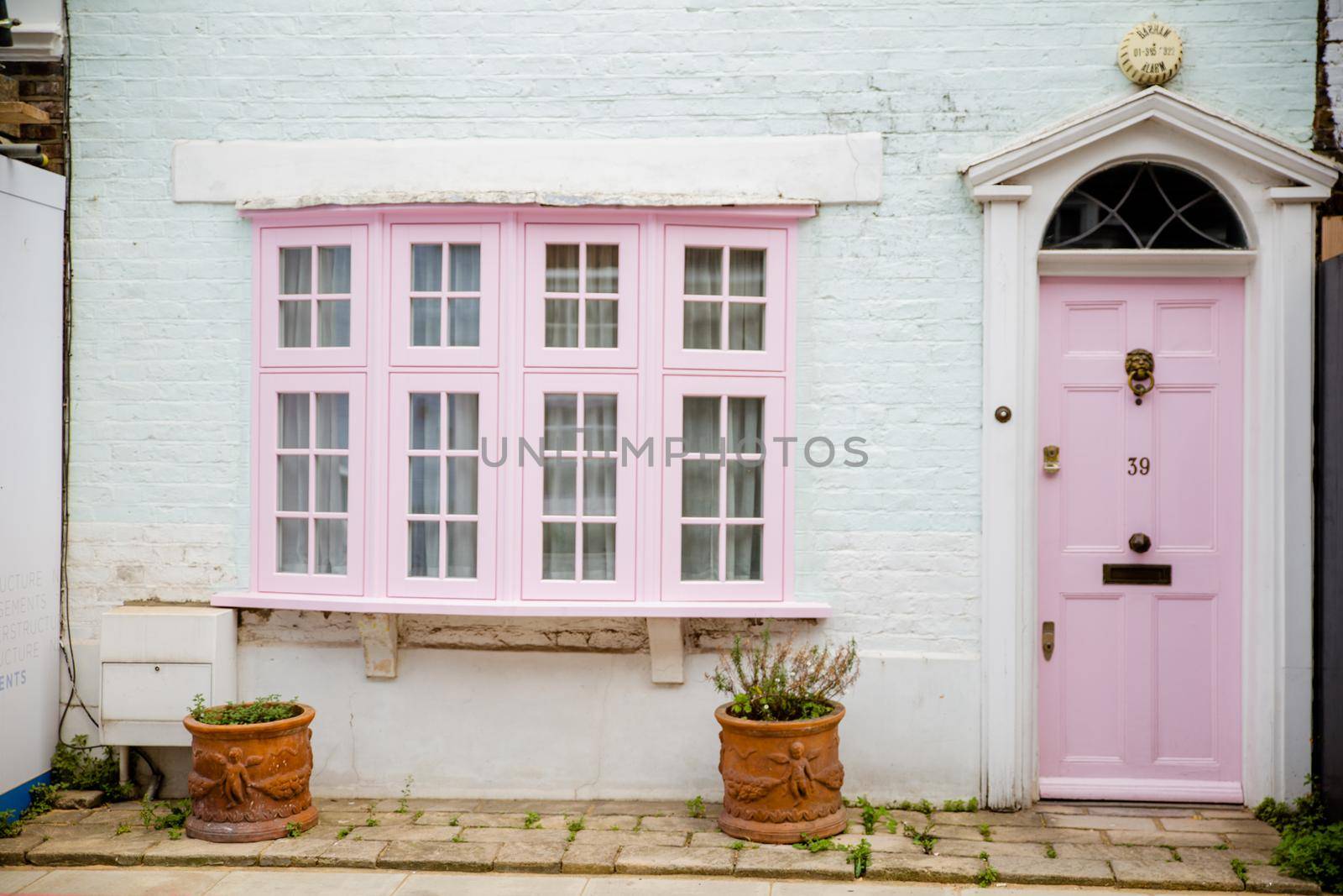 Front side of white and pink British house with empty pots under the window. Beautiful pastel color English house with Victorian architecture. Colorful London neighborhood