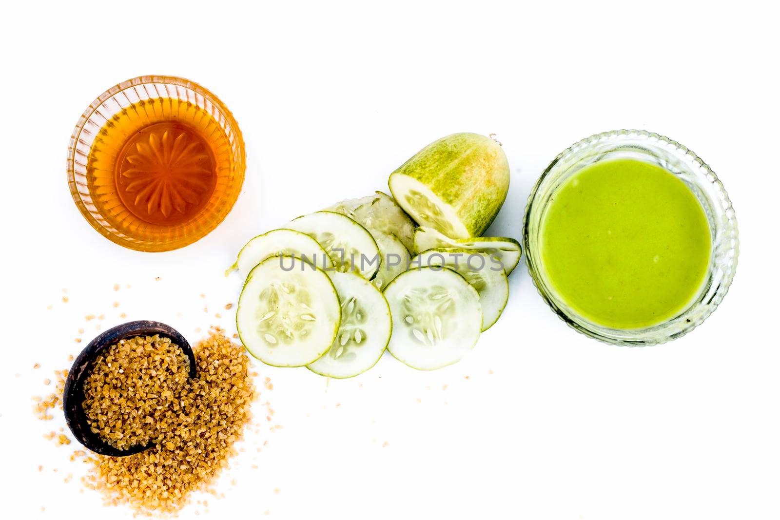 Cucumber face pack isolated on white i.e. Cucumber slices or cucumber pulp well mixed with turmeric powder and some lemon juice in a bowl and entire raw ingredients present on the surface.