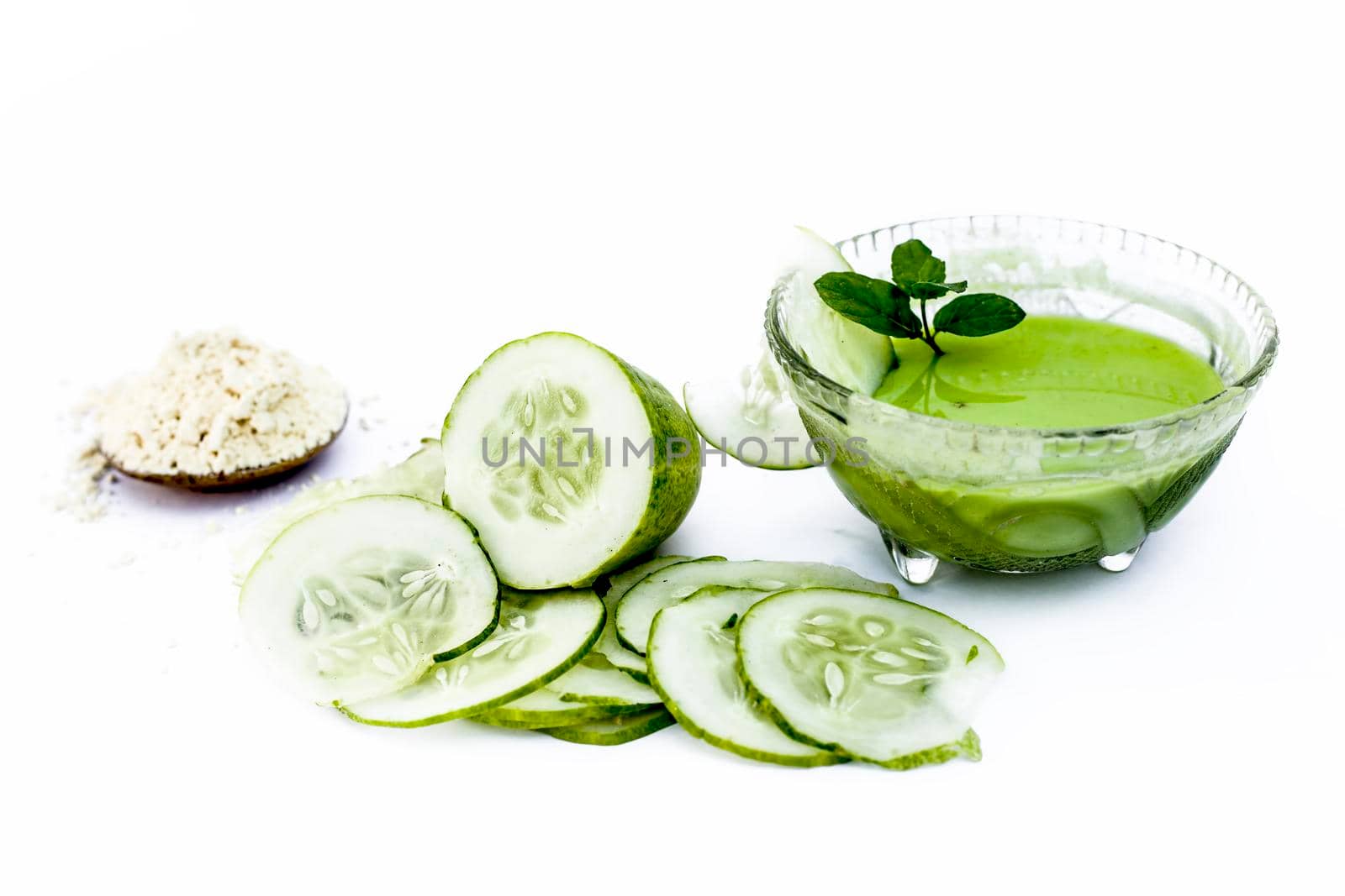 Cucumber face pack isolated on white i.e. Cucumber juice well mixed with gram flour in a glass bowl and all the raw ingredients present on the surface.Used for instant glow.