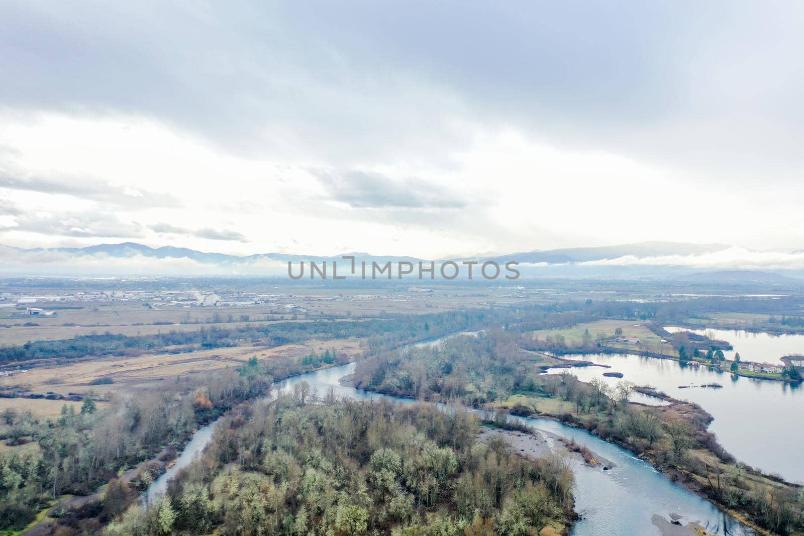 Peaceful rivers surrounding the forest with mountains far in the distance. Beautiful aerial view of rivers going through the woods under cloudy sky. Wooded and rocky landscapes