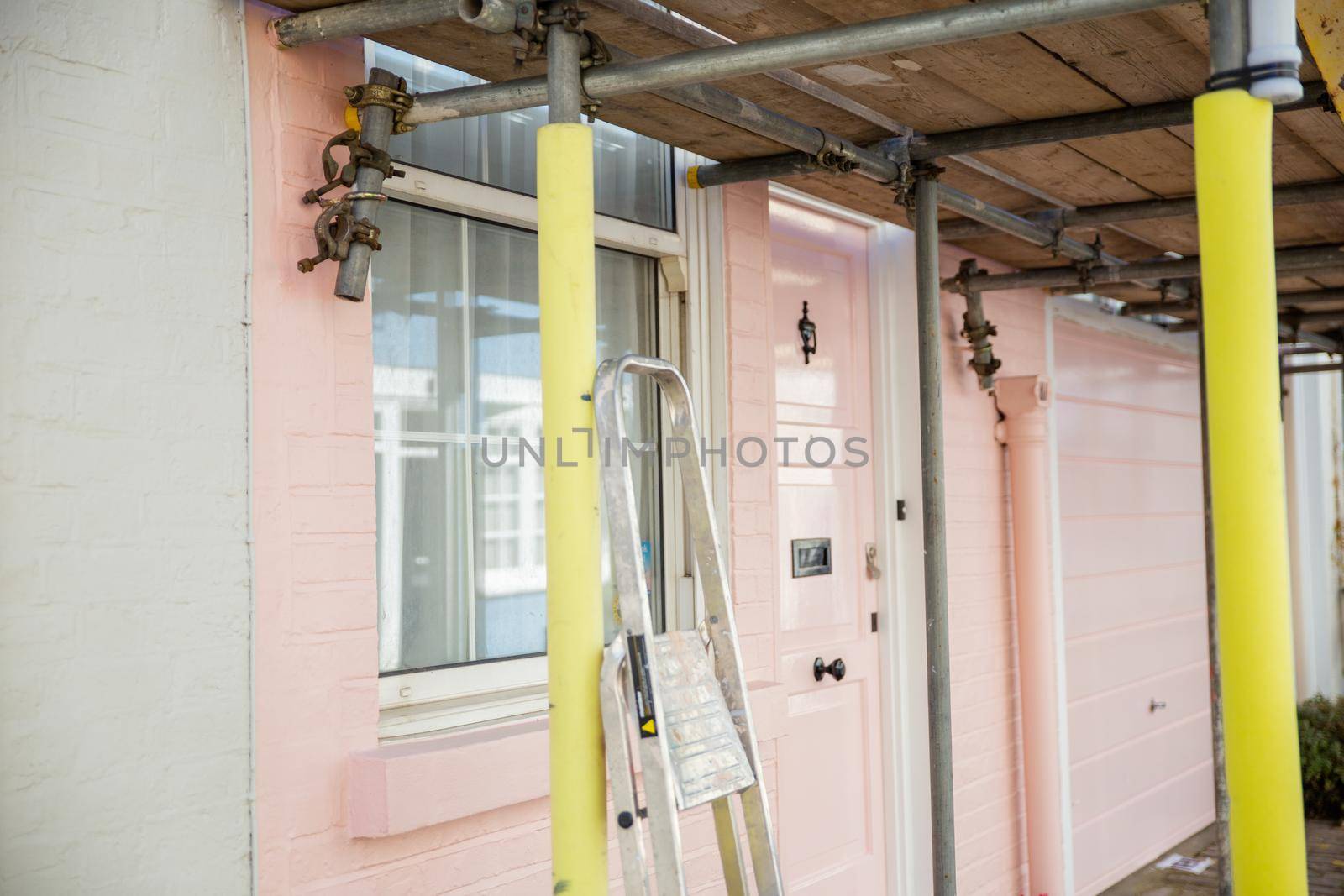 Scaffold outside window and door of pastel pink British house. Beautiful colorful English house behind metal structure. Colorful London neighborhood