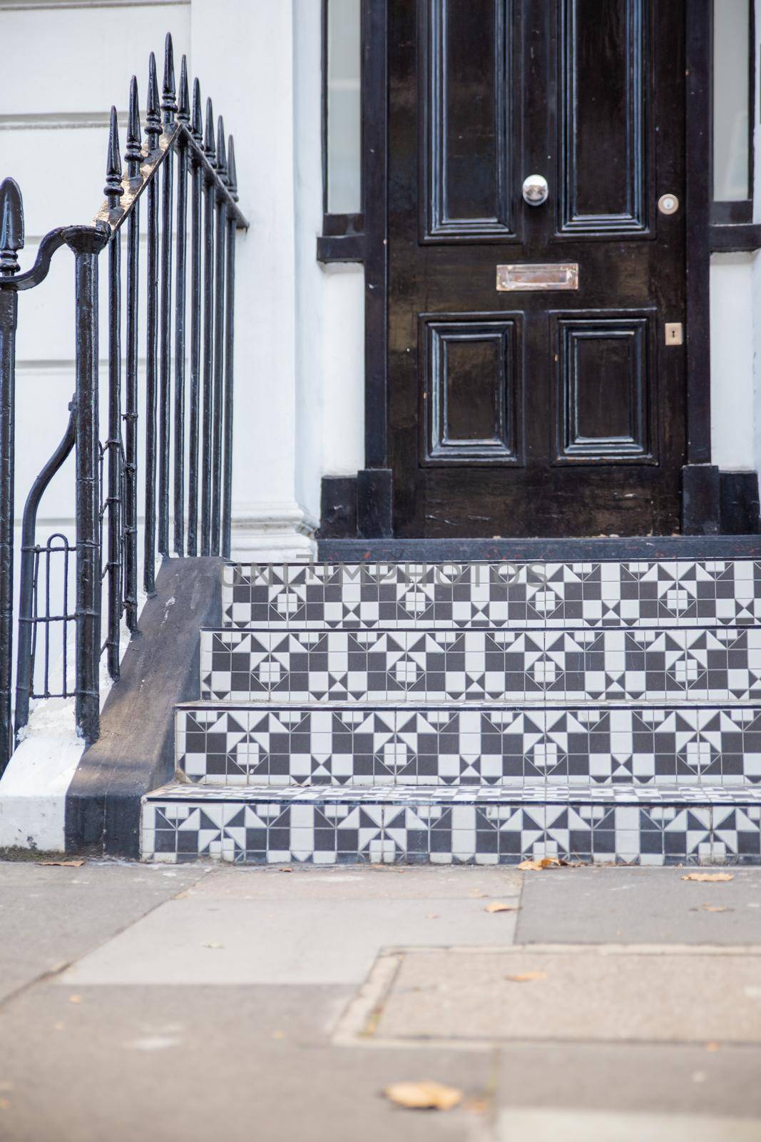 Black and white tiles on the stairs of white British house with black door. Beautiful tiles design on stairs of English house with victorian architecture. Colorful London neighborhood
