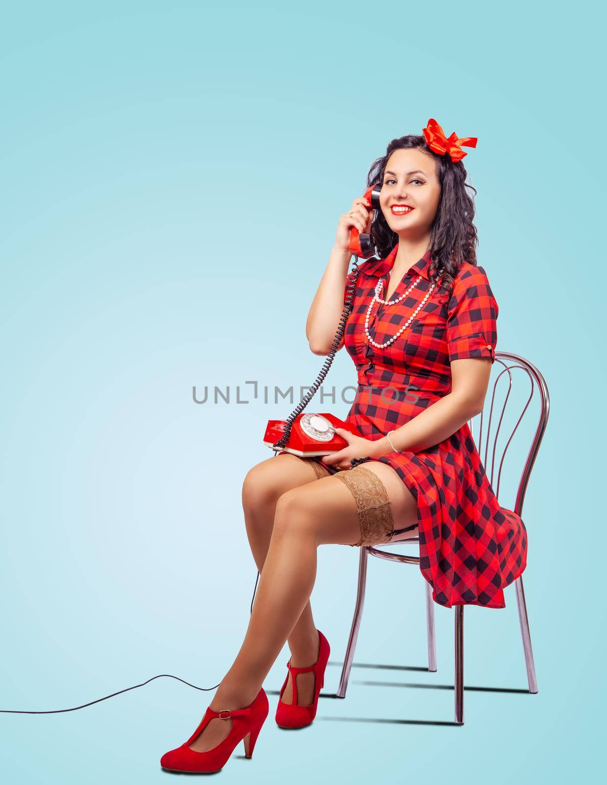 young beautiful woman speaks by phone while sitting on a chair in studio. pinup style