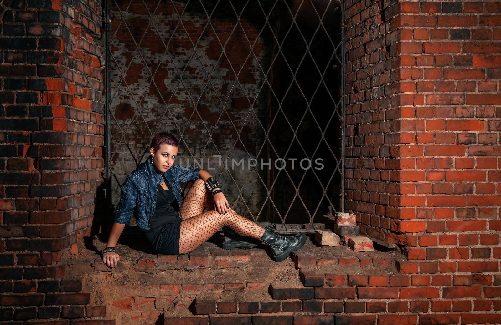 punk girl  sitting in basement of medieval castle near the lattice