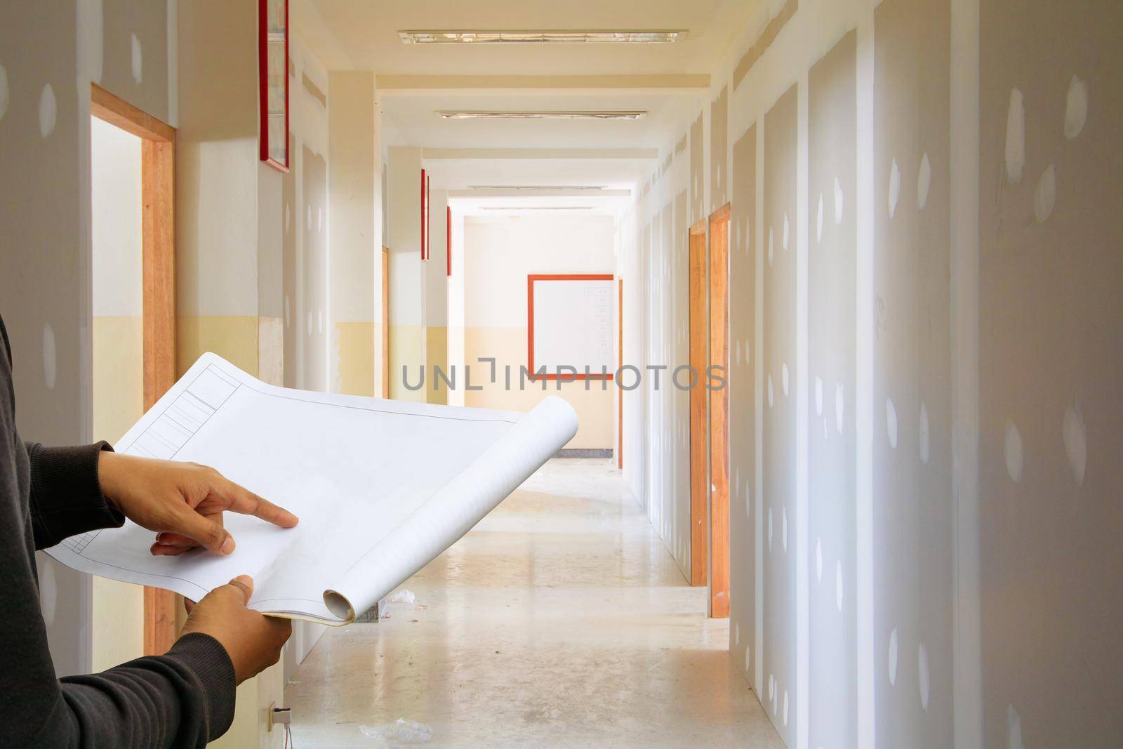 engineer finger point on paper plan blueprint in check building technician place construction site gypsum board wall interior  background by pramot