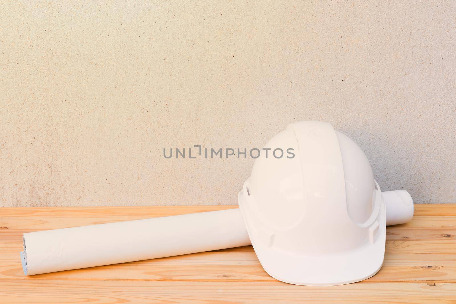 white safety helmet plastic and paper roll plan blueprint construction of engineering on wood floor table background with copy space add text