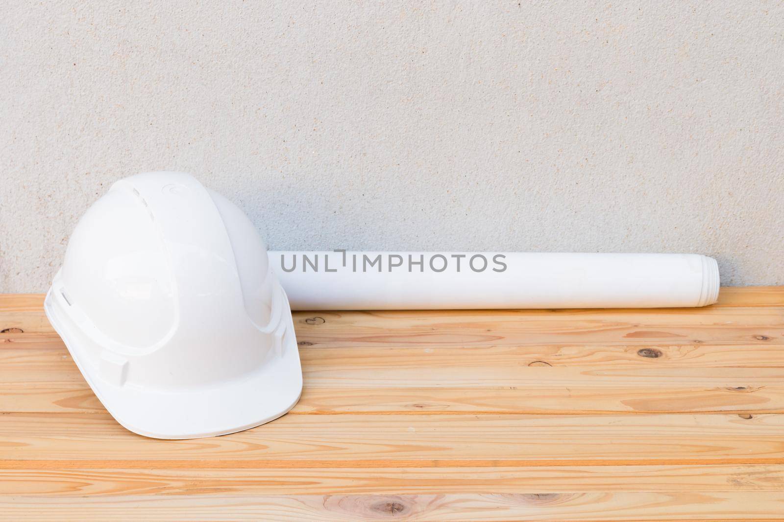 white safety helmet plastic and paper roll plan blueprint construction of engineering on wood floor table background with copy space add text