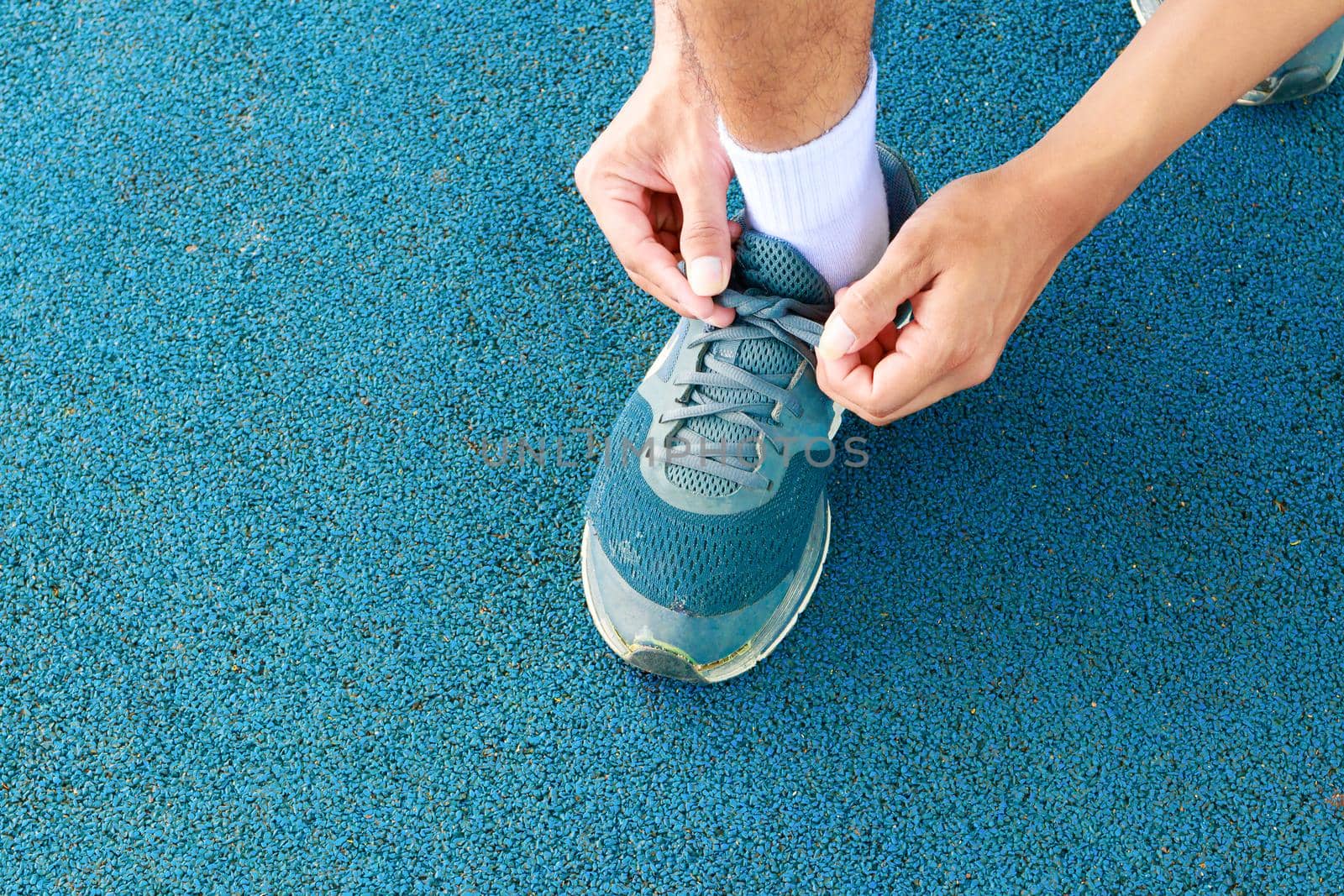 young male runner tying shoelaces old in runner exercise for health lose weight concept on track rubber cover blue public park by pramot