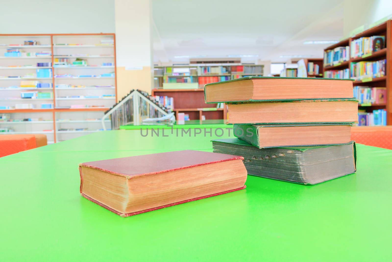 old book and heap treatise in school library on table green. blurry bookshelves background. education learning concept with copy space add text