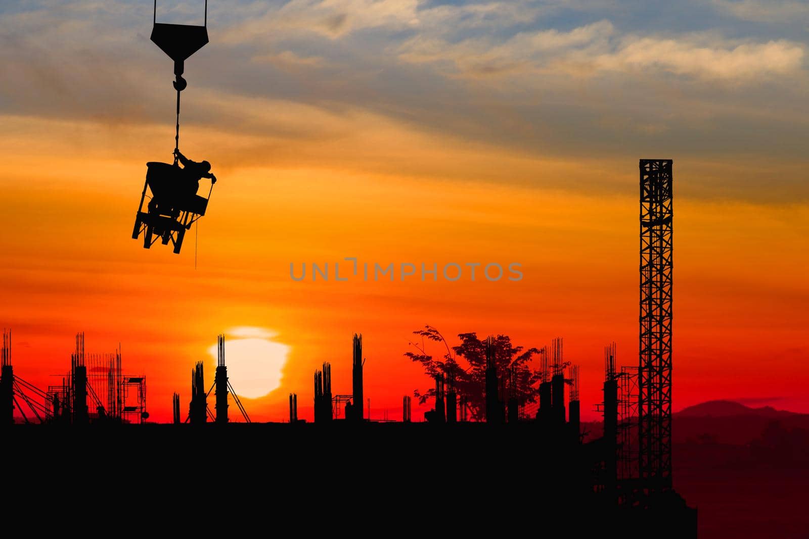 Silhouette construction  worker on crane hook on sunset-sunrise time background by pramot